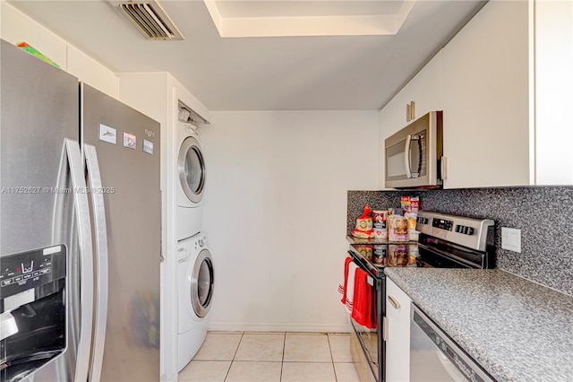 washroom featuring stacked washer and dryer, light tile patterned floors, visible vents, and laundry area