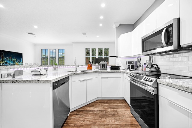 kitchen with stainless steel appliances, white cabinetry, a sink, and a peninsula