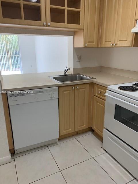 kitchen with white appliances, light tile patterned floors, light countertops, light brown cabinetry, and a sink