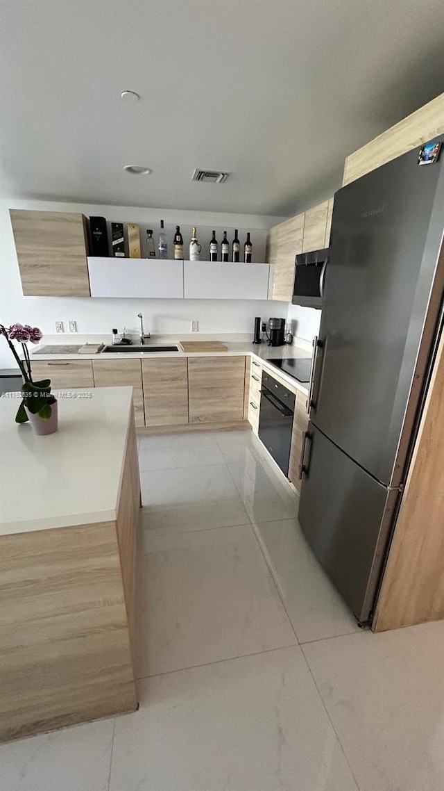 kitchen with light countertops, visible vents, light brown cabinets, modern cabinets, and black appliances