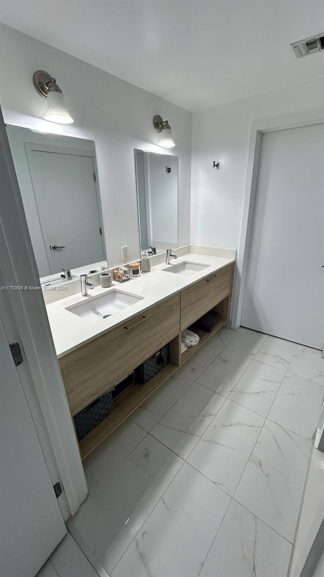 bathroom featuring marble finish floor, double vanity, a sink, and visible vents