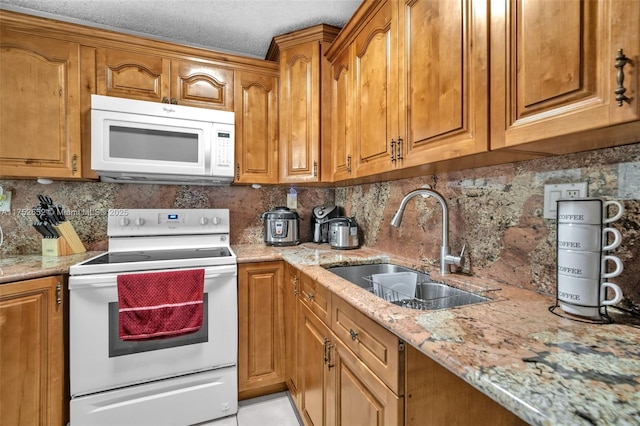 kitchen featuring white appliances, brown cabinetry, a sink, and light stone counters