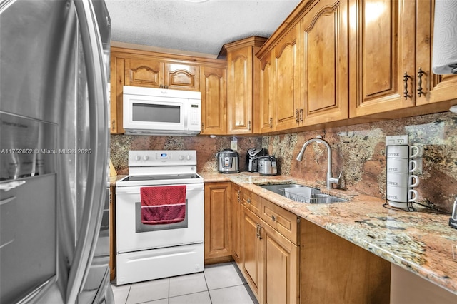 kitchen featuring light stone counters, light tile patterned floors, tasteful backsplash, a sink, and white appliances