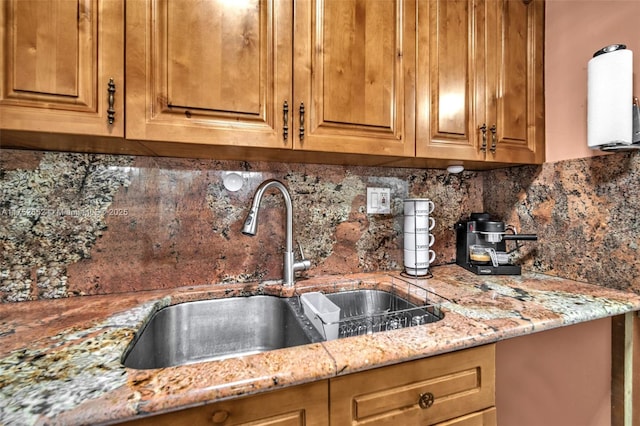 kitchen featuring brown cabinets, light stone counters, a sink, and decorative backsplash