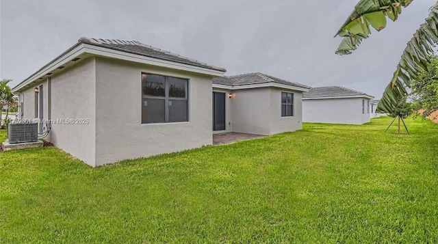 rear view of house with stucco siding, a yard, and central AC unit