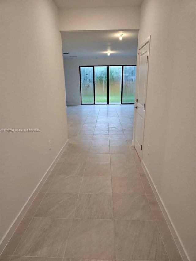 hallway with light tile patterned floors, floor to ceiling windows, and baseboards