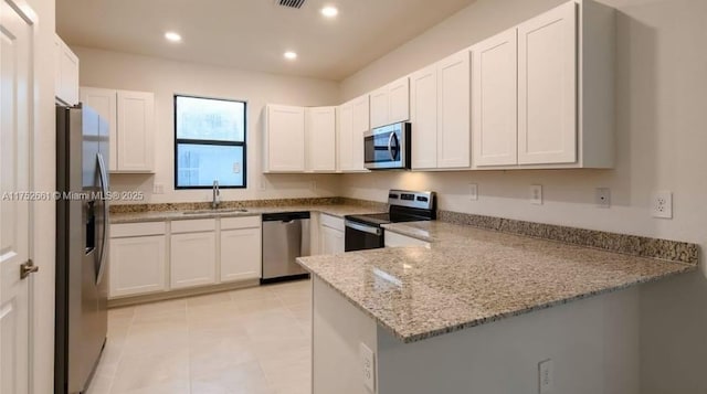 kitchen featuring white cabinets, appliances with stainless steel finishes, light stone counters, a peninsula, and a sink