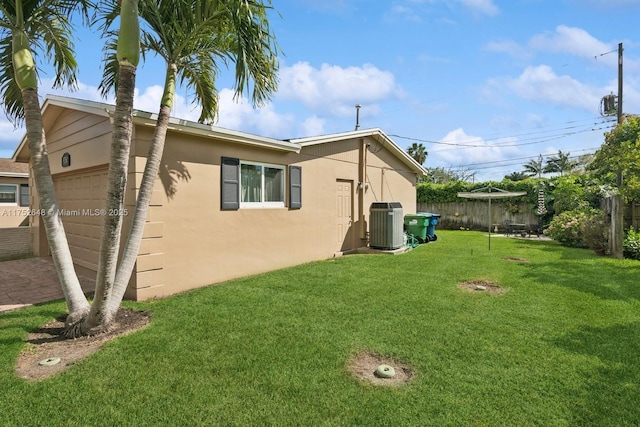 view of home's exterior with a yard, stucco siding, central AC unit, fence, and a garage