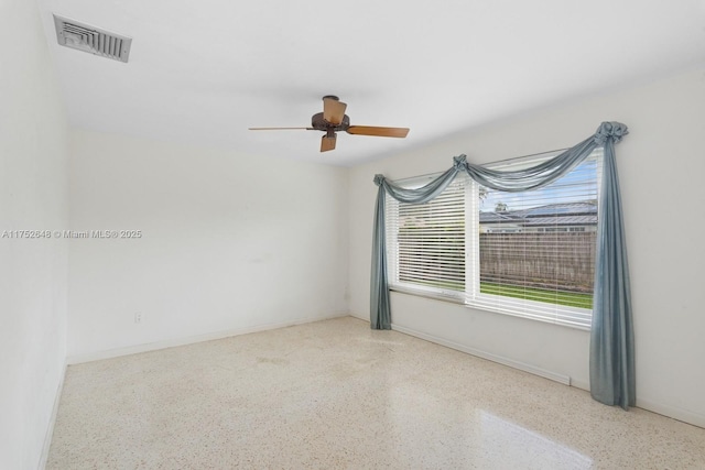 empty room with baseboards, visible vents, ceiling fan, and speckled floor