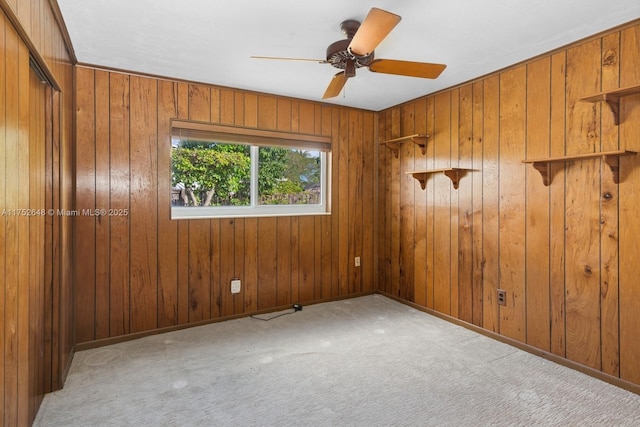 empty room with carpet floors, wood walls, baseboards, and a ceiling fan