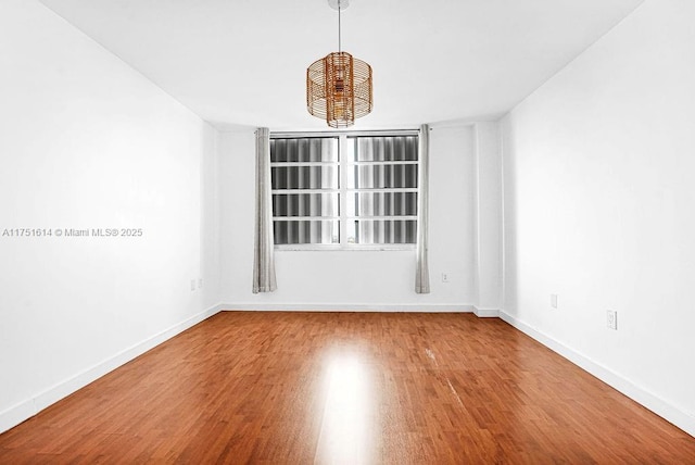 spare room featuring a notable chandelier, baseboards, and wood finished floors