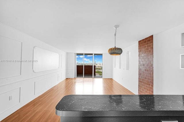 interior space with a decorative wall, a peninsula, hanging light fixtures, light wood-type flooring, and a wall of windows