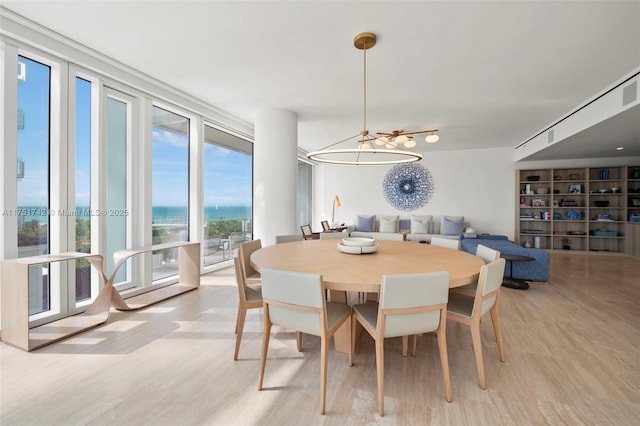 dining room featuring a wall of windows, light wood-type flooring, and a water view