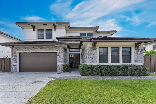 prairie-style home with stone siding, decorative driveway, fence, and a front lawn