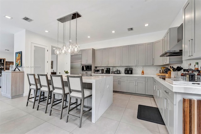 kitchen with visible vents, light countertops, wall chimney range hood, and a kitchen island with sink