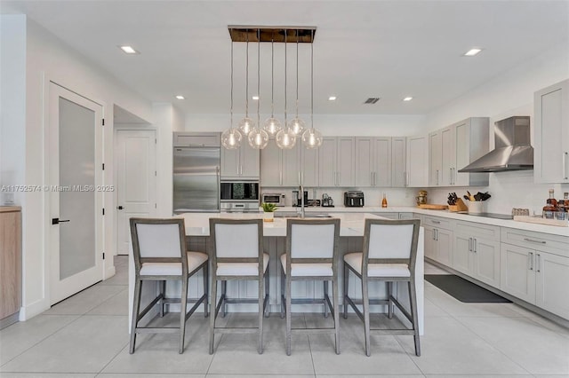 kitchen with a kitchen island with sink, light countertops, and wall chimney range hood