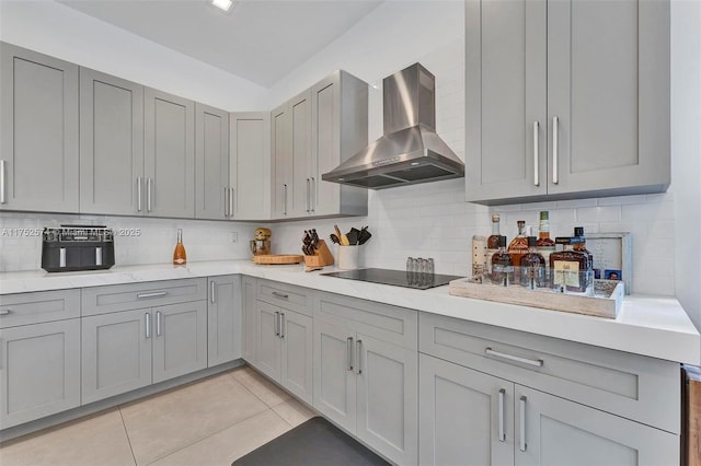 kitchen featuring tasteful backsplash, gray cabinets, black electric cooktop, wall chimney range hood, and light tile patterned flooring