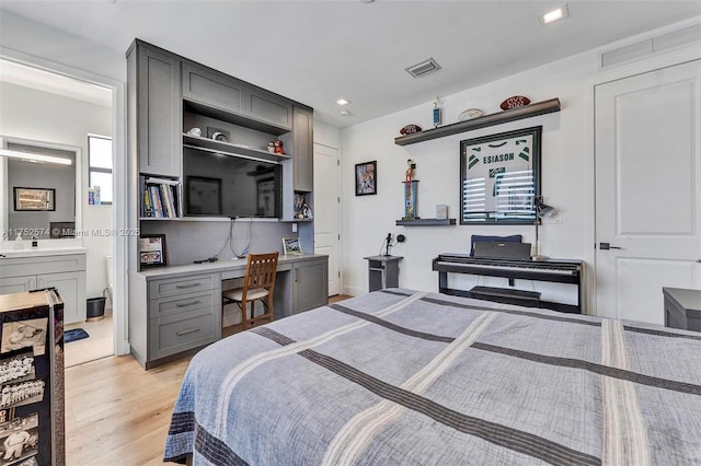 bedroom with light wood-style floors, visible vents, connected bathroom, and built in study area