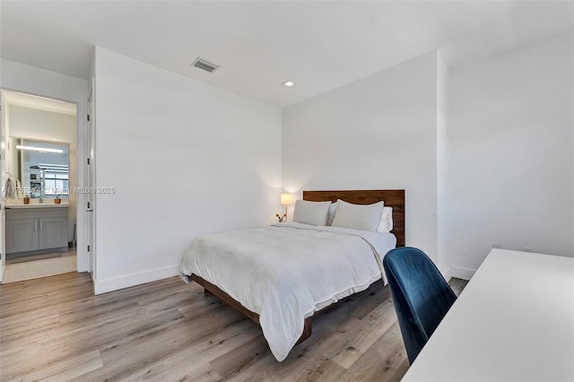 bedroom with light wood-style flooring, connected bathroom, visible vents, and baseboards