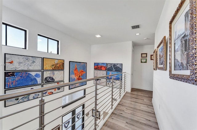 hall with baseboards, visible vents, and light wood finished floors