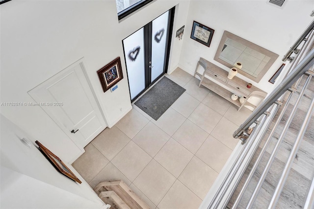 foyer with light tile patterned flooring, a towering ceiling, visible vents, baseboards, and french doors