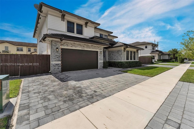 view of front facade with a garage, stone siding, fence, and decorative driveway