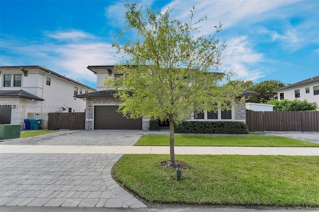 view of front of property with stone siding, an attached garage, fence, decorative driveway, and a front lawn