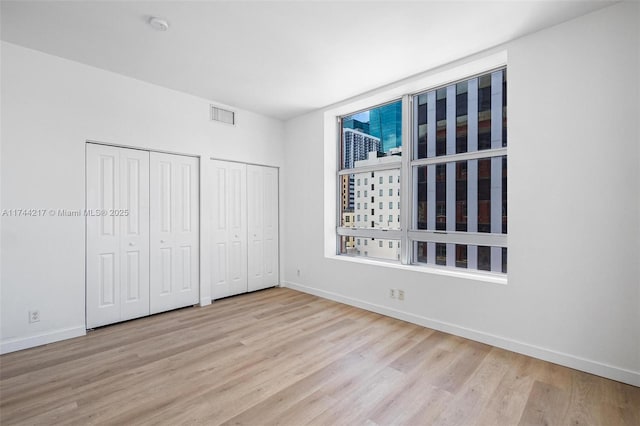 111 E Flagler St Unit 704, Miami, FL 33131 - unfurnished bedroom featuring baseboards, light wood-style flooring, visible vents, and multiple closets