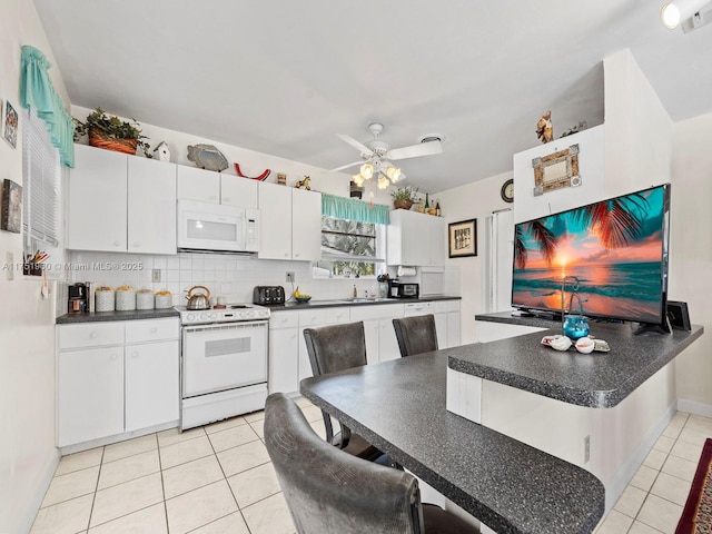 kitchen with dark countertops, white appliances, light tile patterned floors, and white cabinetry