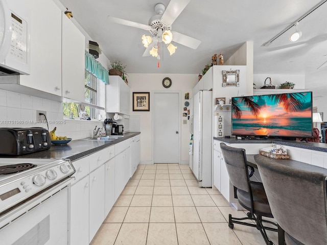 kitchen featuring dark countertops, white appliances, light tile patterned floors, and white cabinetry