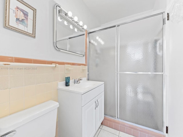 bathroom with wainscoting, toilet, a shower with door, vanity, and tile walls