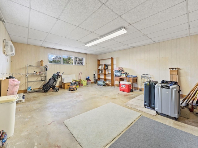 basement featuring wood walls, a drop ceiling, and a wall mounted AC