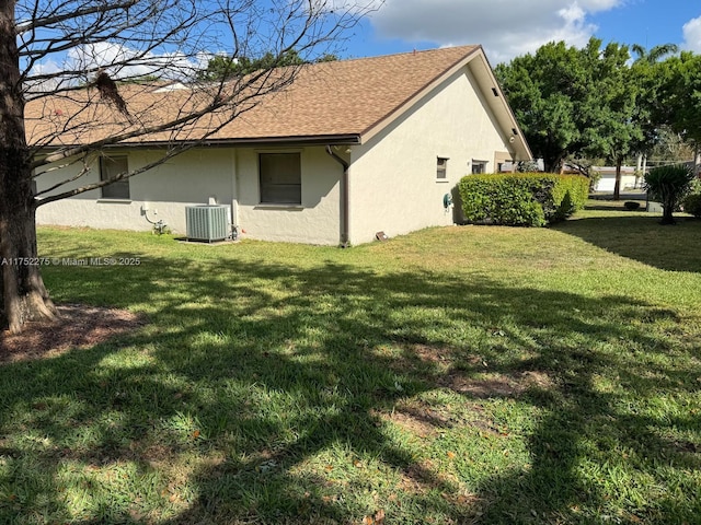 view of side of property featuring a yard, central air condition unit, roof with shingles, and stucco siding