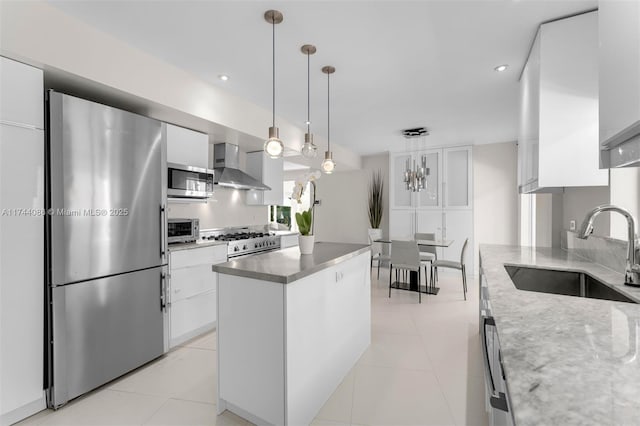 kitchen with stainless steel appliances, a sink, white cabinets, wall chimney range hood, and pendant lighting