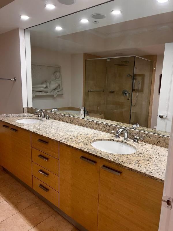 bathroom with double vanity, a sink, a shower stall, and tile patterned floors