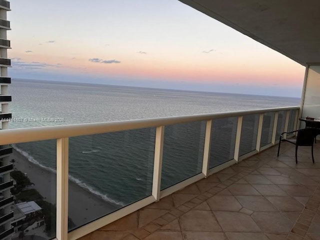 balcony at dusk featuring a water view and a view of the beach