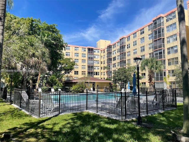 community pool with a patio area, fence, and a lawn