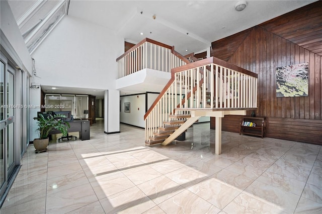 interior space with marble finish floor, wood walls, stairway, and a towering ceiling