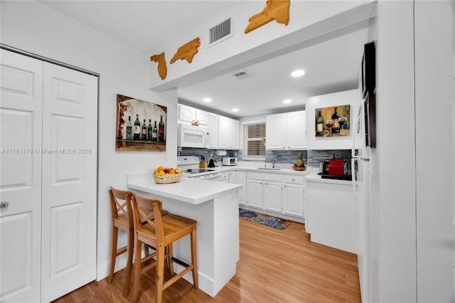 kitchen with a breakfast bar, light countertops, white microwave, stove, and white cabinets