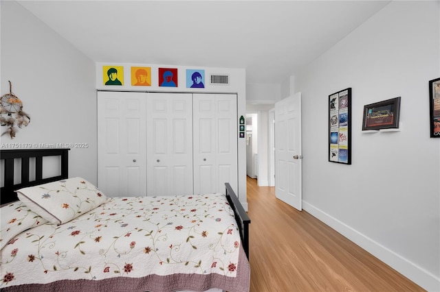 bedroom with light wood finished floors, visible vents, baseboards, and a closet