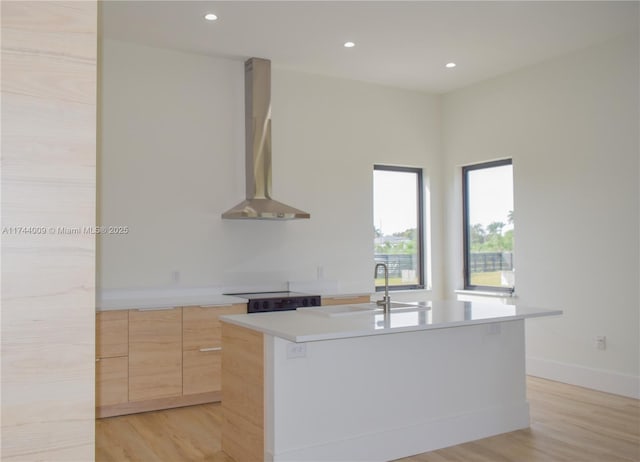 kitchen featuring light brown cabinets, light countertops, wall chimney exhaust hood, light wood finished floors, and modern cabinets