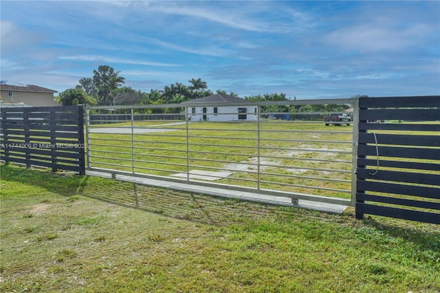 view of gate with a rural view, a lawn, and fence