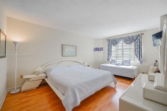 bedroom with a textured ceiling, baseboards, and wood finished floors