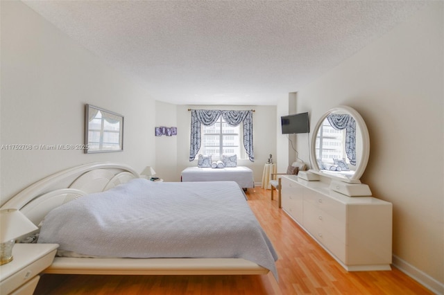 bedroom featuring baseboards, light wood-style flooring, and a textured ceiling