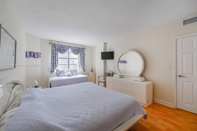 bedroom with baseboards, a textured ceiling, visible vents, and wood finished floors