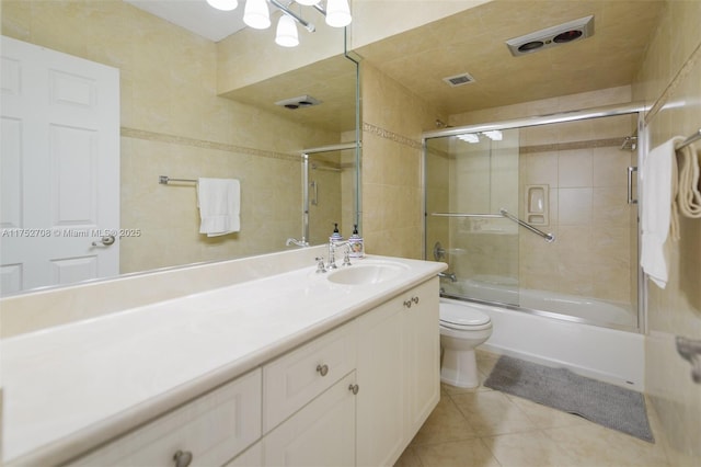 full bathroom featuring bath / shower combo with glass door, visible vents, toilet, vanity, and tile patterned floors