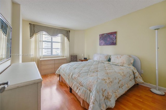 bedroom with light wood-style flooring, baseboards, and a textured ceiling