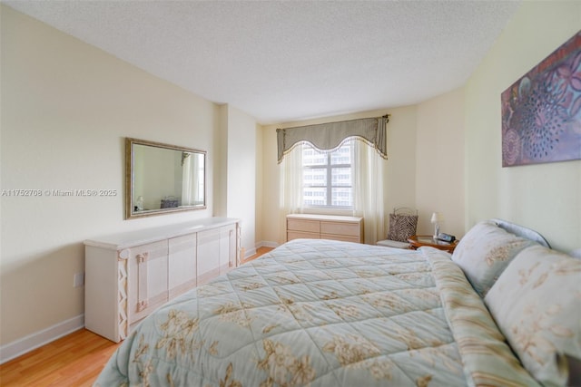 bedroom with light wood-type flooring, a textured ceiling, and baseboards