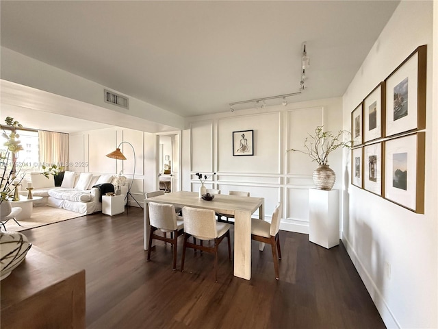 dining area with dark wood-style floors, visible vents, a decorative wall, and track lighting