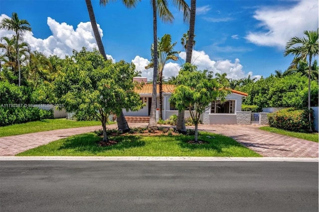 view of front facade featuring decorative driveway, a tile roof, stucco siding, a front yard, and fence